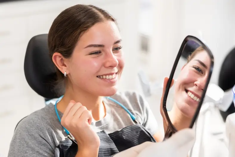 Patient checking smile in mirror, showing results of cosmetic dentistry