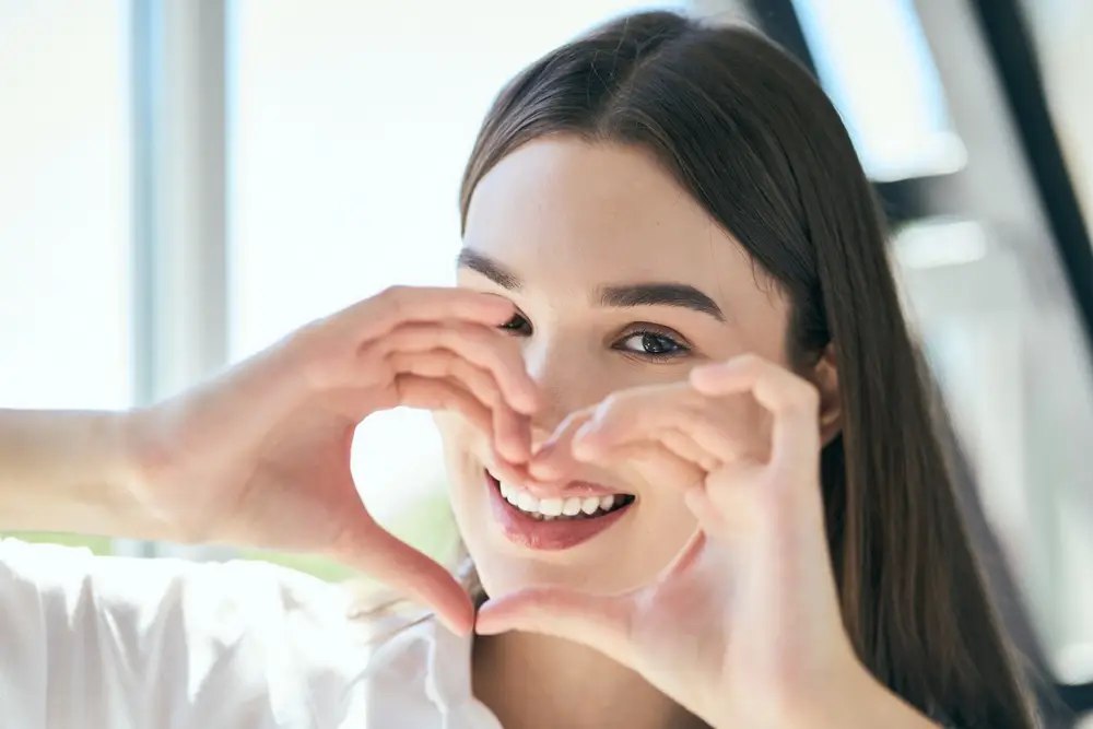 Woman making heart shape with hands, satisfied with teeth whitening at Hill Avenue Dental